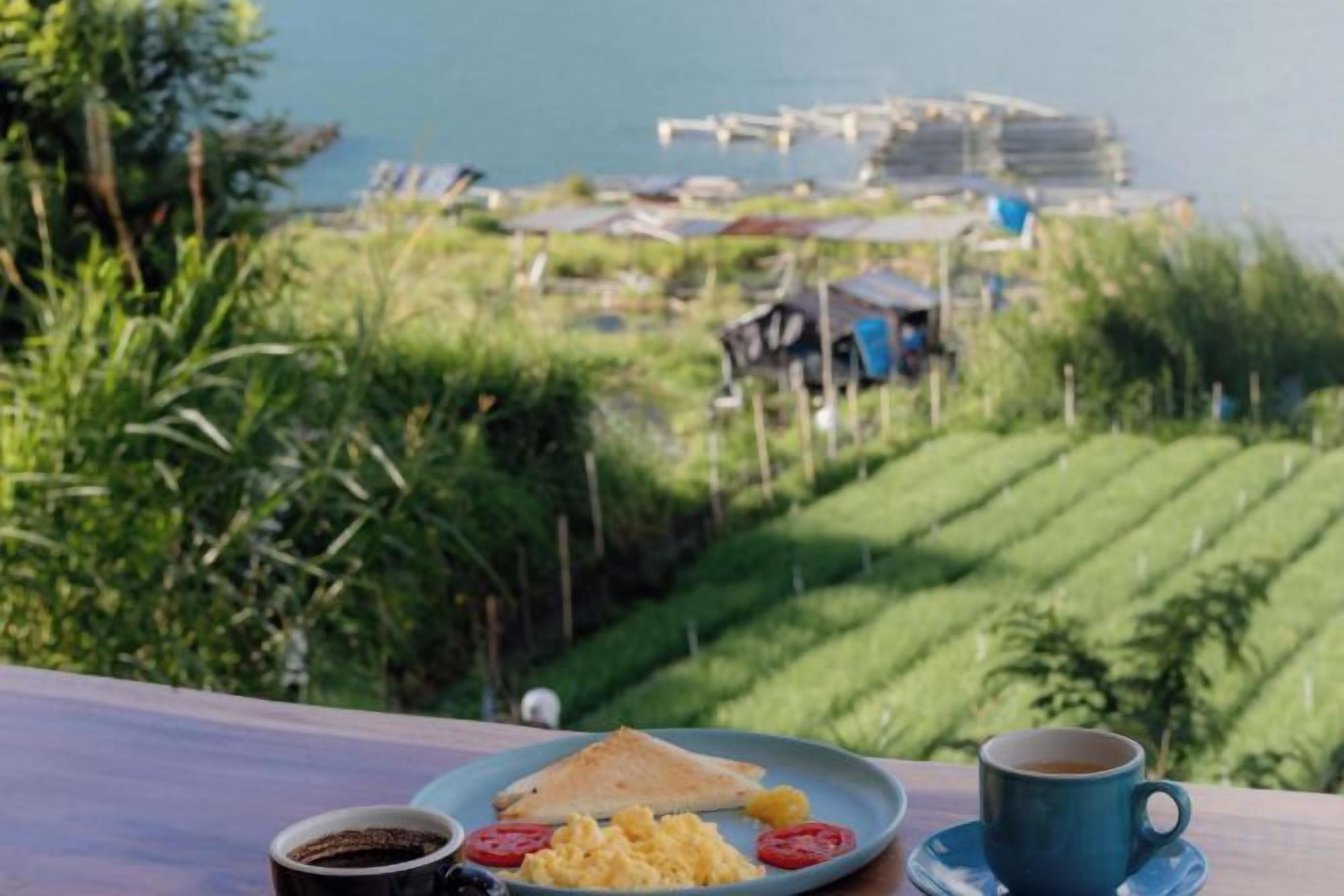 A meal with a plate, a cup, and a bowl on a table with a view of a water body and greenery.