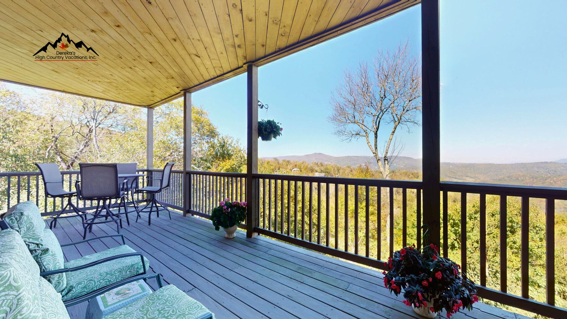 A covered outdoor deck with seating and potted plants, overlooking a mountainous landscape.