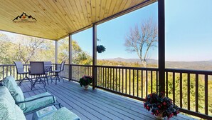 Eine überdachte Terrasse im Freien mit Holzboden, einem Tisch mit Stühlen und Blick auf eine Berglandschaft.
