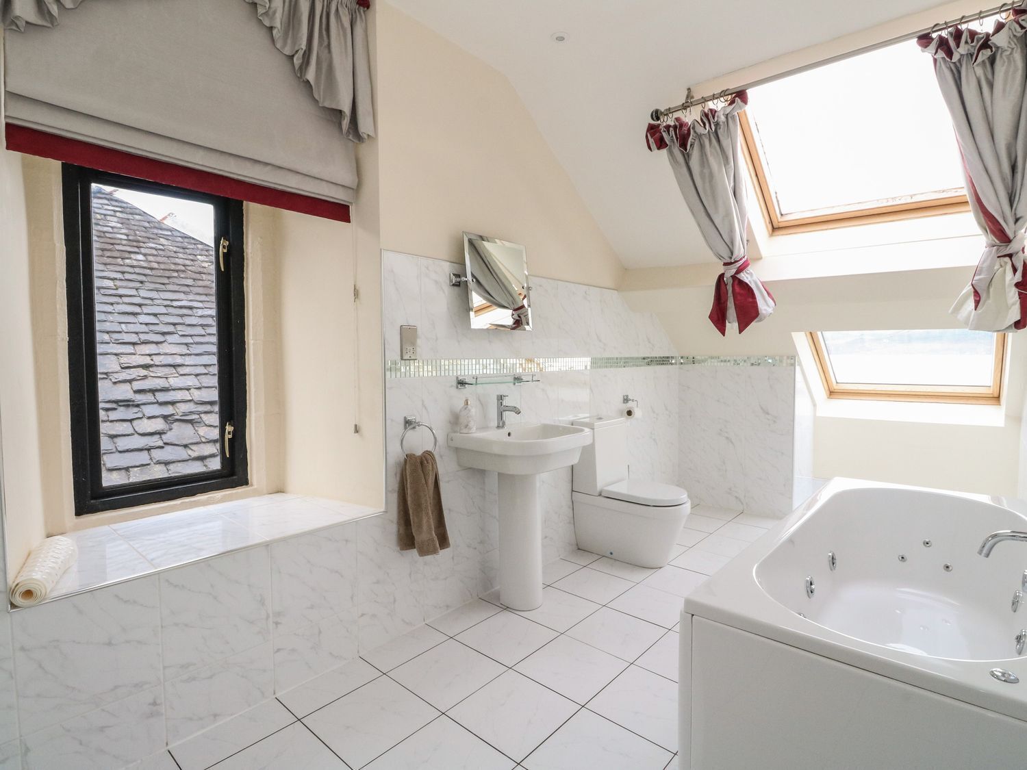 Un baño moderno con una bañera grande, un lavamanos y un inodoro. Hay una ventana con cortinas y vistas al exterior.