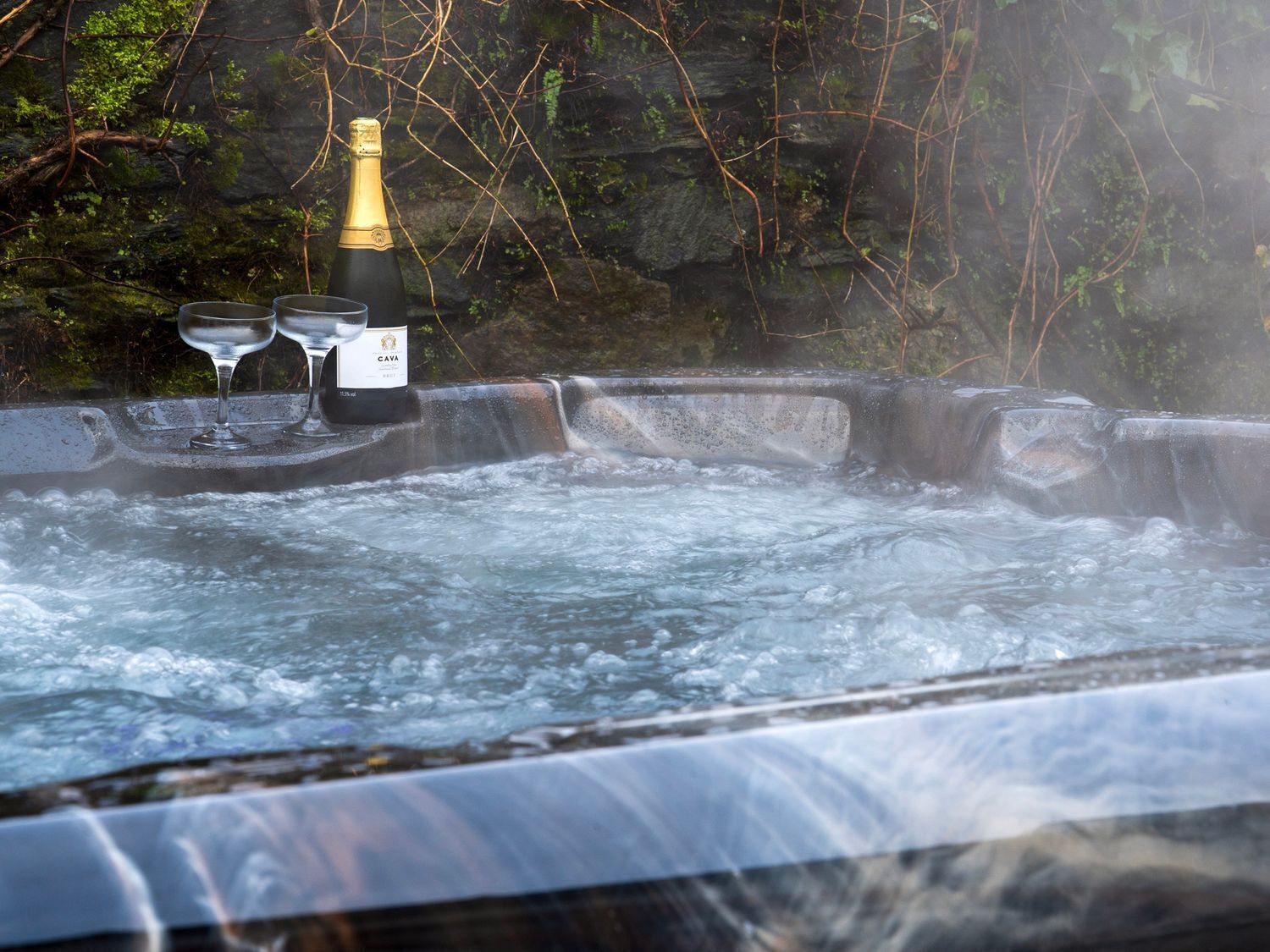 Una vasca idromassaggio con una bottiglia di CAVA e due bicchieri.