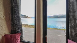 A room with a large window offering a view of a lake and distant hills. - Newton Hall (Inveraray)