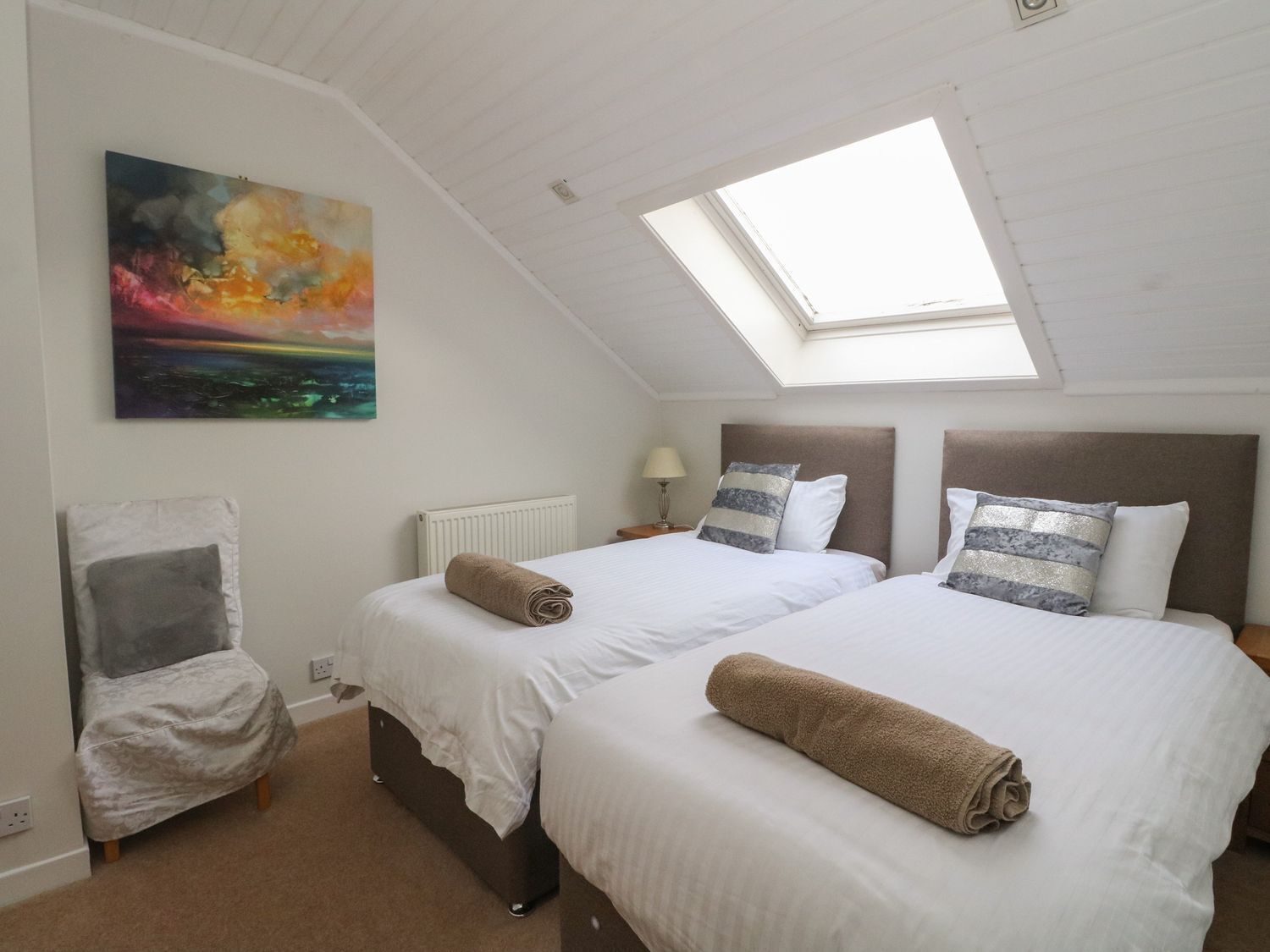 Une chambre avec deux lits, une lucarne, un tableau et une chaise.