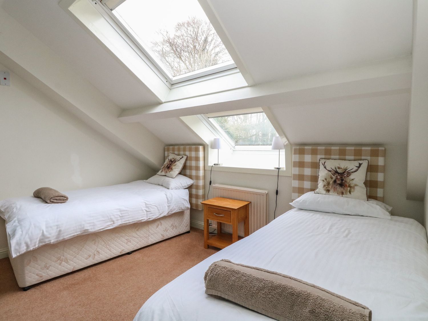 A small, cozy attic bedroom with two single beds, a wooden nightstand, and a skylight.