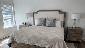 A bedroom with a bed, a ceiling fan, two bedside tables with lamps, and a window with blinds.