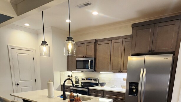 A modern kitchen with a central island, stainless steel appliances, and wooden flooring.