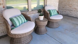 A covered patio area with wicker furniture and a potted plant.