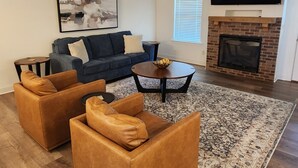 A living room with a fireplace, a ceiling fan, and a large TV.
