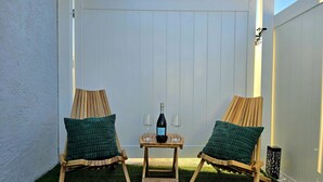 Two wooden chairs with green cushions, a small table with a bottle of wine and two glasses, and a white fence in a backyard with artificial grass. - Right Apt 1 BR, 7` TPA Airport, 14` Ray Jam, Pkng (Tampa)