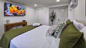 A modern bedroom with a large bed, a TV mounted on the wall, a bedside table, and a door leading to another room. - Right Apt 1 BR, 7` TPA Airport, 14` Ray Jam, Pkng (Tampa)