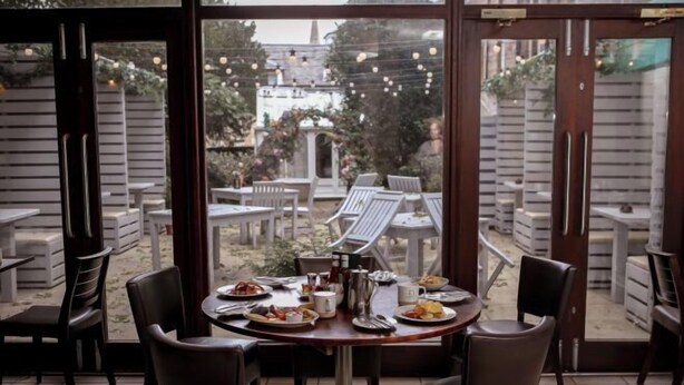 A dining area with a table set for two, surrounded by chairs, and a view of an outdoor patio with tables and chairs. - Bruntsfield Hotel, WorldHotels Elite (Edinburgh)