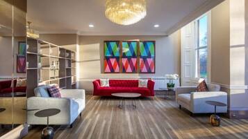 A modern living room with a red sofa, white sofas, a chandelier, and colorful artwork on the wall.