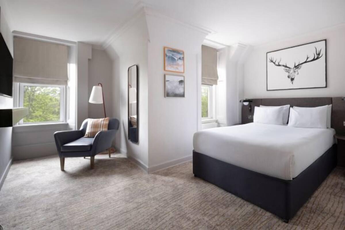 A hotel room with a large bed, a chair, a desk, and a window with a view.