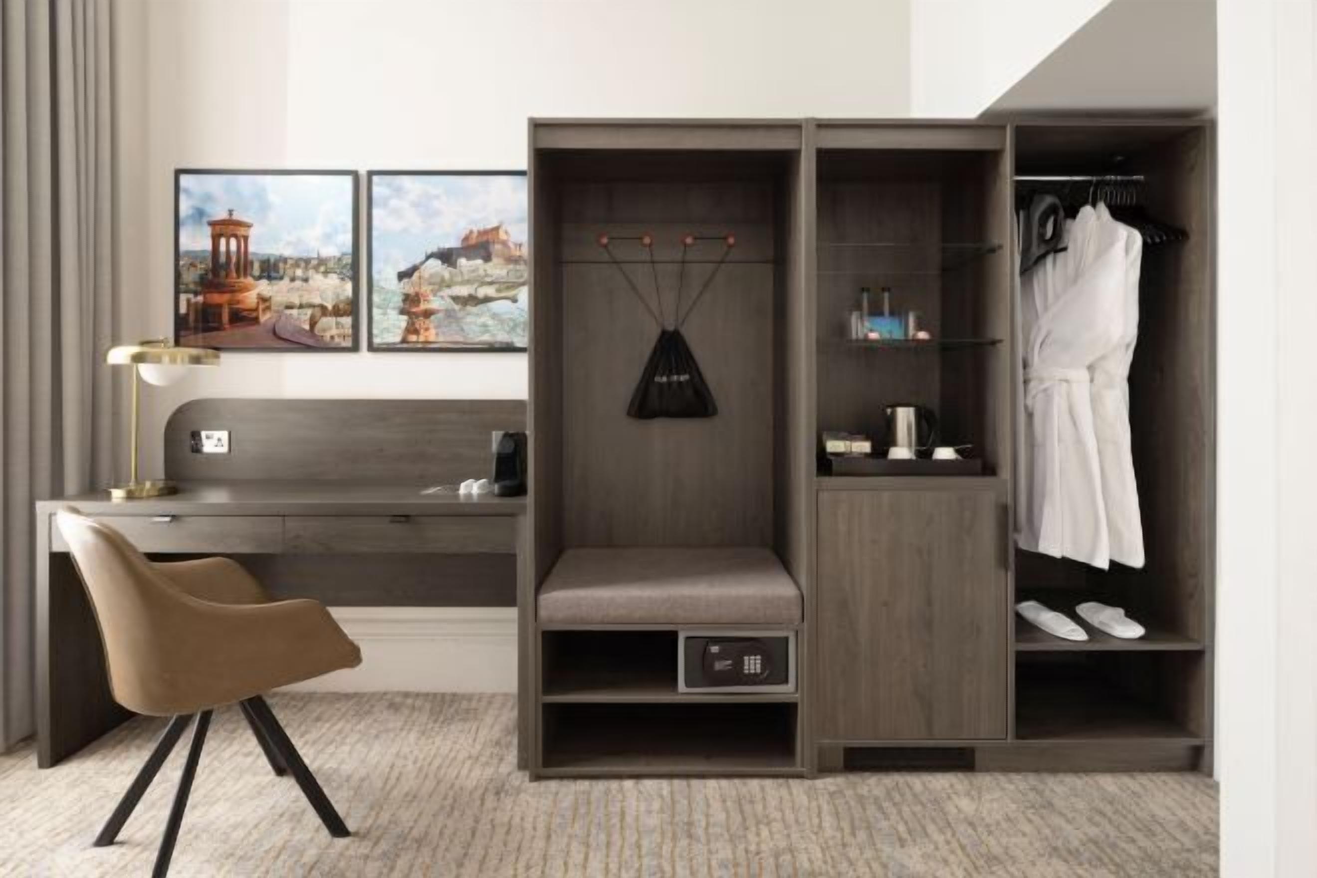 Een moderne hotelkamer met een bureau, een bankje, een garderobe en een schoenenrek.