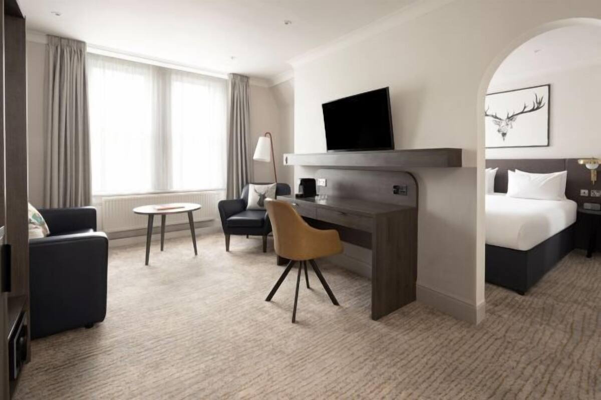 A hotel room with a bed, a desk, a chair, a television, and a window with curtains.