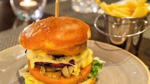 A burger with a toasted bun, cheese, lettuce, tomato, and a meat patty, served on a plate with a side of fries. - Bruntsfield Hotel, WorldHotels Elite (Edinburgh)