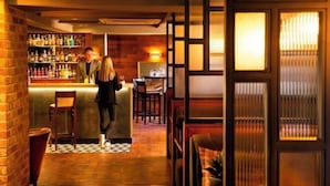 A bar area with a brick wall, wooden floor, and a bar counter with bottles. There are chairs and tables in the background. - Bruntsfield Hotel, WorldHotels Elite (Edinburgh)