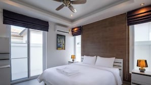 A modern hotel room with a large bed, a ceiling fan, a window with a view, and a nightstand with a lamp. - Orchid Paradise Homes OPV 213 (Hua Hin)