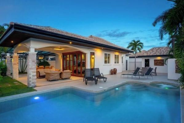A modern house with a swimming pool, outdoor seating, and a covered patio.