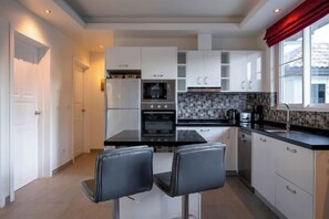 A modern kitchen with white cabinets, a black countertop, and two bar stools.