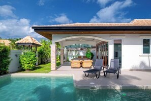 A poolside area with lounge chairs, a covered patio, and a view of the pool.