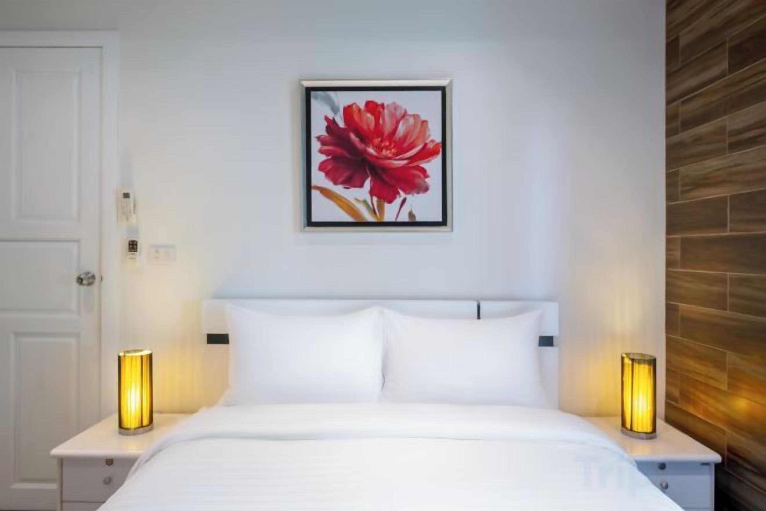 A hotel room with a bed, two bedside tables, and a framed picture on the wall.
