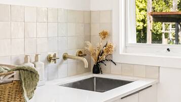 A modern laundry room with a Bosch washing machine, a window with a view of greenery, and a white tiled backsplash.
