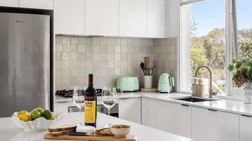 A modern kitchen with a stainless steel refrigerator, a wine bottle, glasses, and a bowl of fruit on the counter.