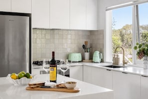 Cocina moderna con un refrigerador de acero inoxidable, una botella de vino, vasos y un cuenco de fruta en la encimera.