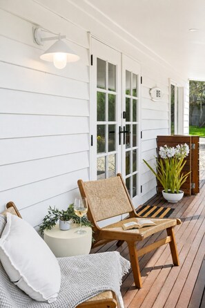 A wooden deck with a wicker chair, a small table with a glass of wine, and a potted plant. - The Rye Bathhouse | Sauna, Outdoor Bath + Fire Pit! (Rye)