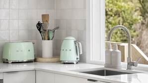 Una cocina con armarios blancos, un tostador, un hervidor y un lavabo con grifo.