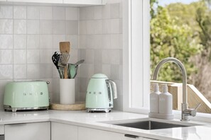 A kitchen with white cabinets, a toaster, a kettle, and a sink with a faucet.
