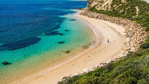 Un paisaje costero con playa despejada, costa rocosa y un camino sinuoso.