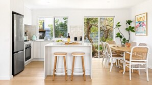 Una cocina moderna con una isla central, taburetes de bar y una zona de comedor con sillas blancas.