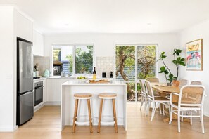 A modern kitchen with a central island, bar stools, and a dining area with white chairs.