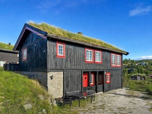 A two-story wooden house with a grass roof, red-framed windows, and a stone foundation.