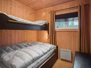 A bunk bed with a mattress and a heater, wooden walls, a window with curtains, and a small table. - Mountain Cabin in Aurdal  Fireplace  Sauna 1000m (Nord-Aurdal)