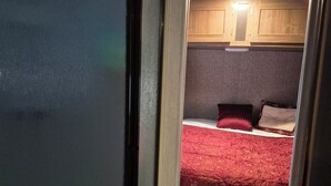 Un pasillo estrecho que conduce a un dormitorio con colcha roja, armarios de madera y una lámpara en el techo.