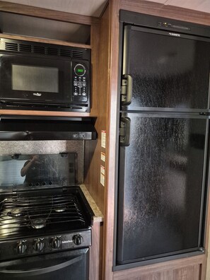 A kitchen with a black microwave, a stove, and a black refrigerator. - Cozy RV in Delightful Fort Walton Beach with AC (Fort Walton Beach)