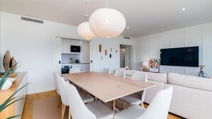 A modern living room with a wooden dining table, white sofas, and a flat-screen TV mounted on the wall. - Miraflores Modern Apt w/ Balcony by LovelyStay (Algés)