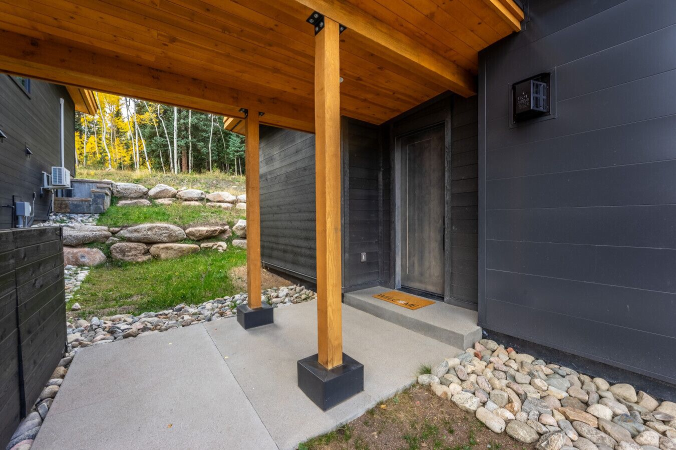 A modern building with a wooden deck, a stone wall, and a metal door.