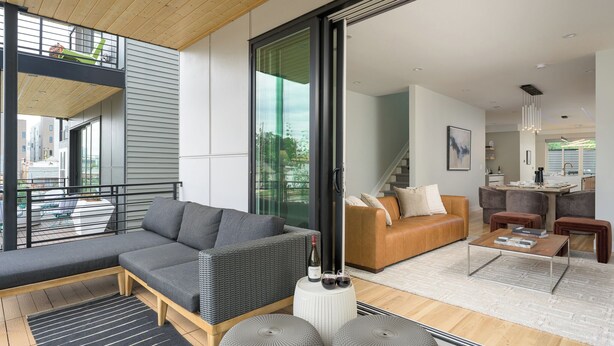 A modern living room with a grey sofa, a wooden bench, and a coffee table. There is a staircase leading to an upper level. - Brand New Luxury Marquee Inn (Denver)