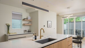 A modern kitchen with a central island, a built-in sink, and a dining area with a table and chairs. - Brand New Luxury Marquee Inn (Denver)