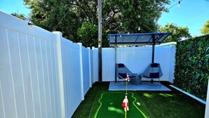 A backyard with artificial turf, a flag, and a covered seating area. - Left Apt.2BR| 7` TPA Airport| AC| Pkng| Wine| HSIA (Tampa)