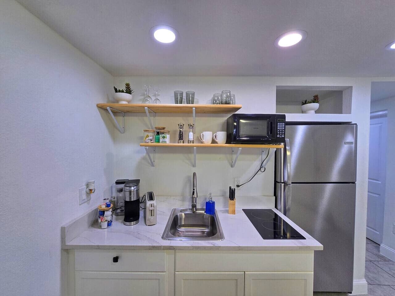 Eine kompakte Küche mit einem Edelstahlkühlschrank, einer Mikrowelle, einem Spülbecken und einer Arbeitsplatte mit verschiedenen Gegenständen.