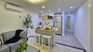 A compact living space with a kitchenette, a dining area with stools, a grey sofa, and a small potted plant. - Left Apt.2BR| 7` TPA Airport| AC| Pkng| Wine| HSIA (Tampa)