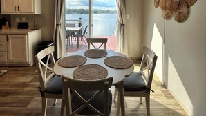 A dining area with a table set for four, a view of the sea, and a kitchen with cabinets.