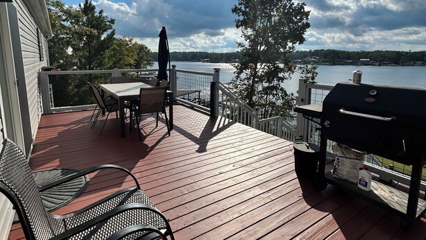 A wooden deck with outdoor furniture, a grill, and a view of a lake.