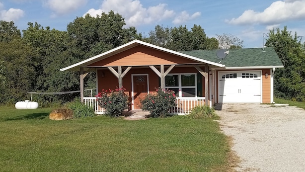 A single-story house with a porch, a garage, and a gravel driveway. - Cozy cabin in remote Appanoose county Iowa a wildlife Mecca (Moravia)