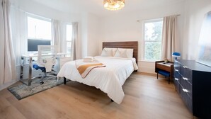 Ein modernes Hotelzimmer mit einem großen Bett, einem Schreibtisch mit Stuhl, einem Schminktisch und einer Pendelleuchte.